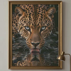 May include: A framed wall art print featuring a close-up portrait of a leopard with golden fur and black rosettes. The leopard is shown drinking from a dark water source, with its face and tongue visible, creating a clear reflection below.