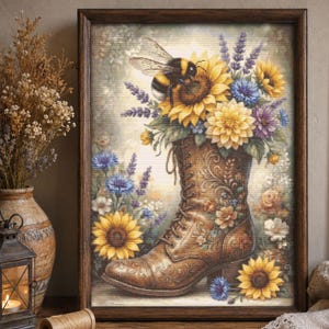 May include: A framed cross-stitch artwork depicting a brown leather lace-up boot filled with a vibrant bouquet of sunflowers, lavender, and blue cornflowers. A large bumblebee rests on a sunflower, all set against a soft, light-colored background.