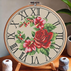 May include: A round embroidery hoop with a beige background and Roman numerals around the edge. The center of the hoop features a floral design with red roses, pink flowers, and green leaves.
