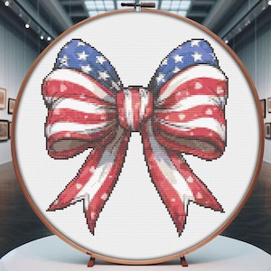 Pode incluir: Um laço vermelho, branco e azul com bolinhas brancas, no estilo da bandeira americana, é exibido em um aro de bordado redondo.