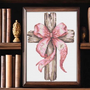 Puede incluir: Una cruz de madera desgastada con un gran lazo rosa atado alrededor. La cruz está enmarcada en un marco de madera marrón.