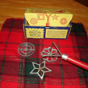 May include: A set of three vintage metal rosette cookie cutters in a red and green plaid box. The cutters are shaped like a star, a flower, and a circle with a cross in the center. The box is labeled "Double Dip Rosette Iron and Timbale Iron Patty Shell."