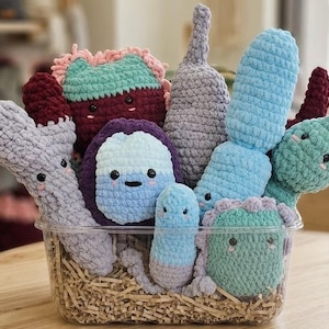 Op de afbeelding: Een verzameling gehaakte knuffels in de vorm van diverse micro-organismen, waaronder bacteriën en virussen in tinten blauw, paars, groen en bordeauxrood. Elk knuffeltje heeft kleine zwarte veiligheidsoogjes en geborduurde roze wangen.