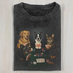 Könnte beinhalten: Dunkelgraues T-Shirt mit einer Pokerszene mit Hunden und einer Katze. Die Grafik zeigt einen Golden Retriever, einen Boston Terrier, eine getigerte Katze und andere Hunde, die Poker um einen grünen Filztisch mit Karten und Chips spielen.