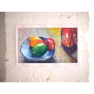 May include: Watercolor painting of a still life featuring a blue plate with an orange, a green lime, and a red apple. A red rectangular object is to the right. The painting is on textured paper.