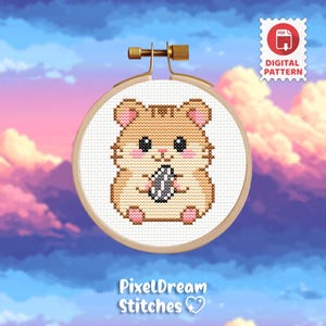 Puede incluir: Patrón de punto de cruz de un hámster sosteniendo una semilla de girasol, en un bastidor de bordado de madera. El hámster es marrón claro con detalles rosas. El texto "PixelDream Stitches" está en la parte inferior. Un icono de patrón digital está en la esquina superior derecha.