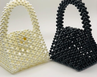 May include: Two small beaded handbags, one white and one black. Both bags have a top handle and are made of small round beads.