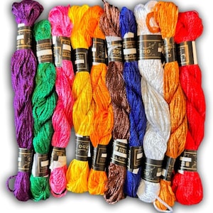 May include: A selection of vibrant embroidery threads in a range of colours: purple, green, pink, yellow, orange, brown, blue, white, and red. Each skein is wrapped with a black and white label. Suitable for cross-stitch, embroidery, and other needlecrafts.