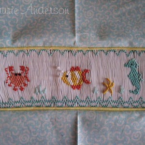 May include: Embroidered fabric panel featuring a sea life design. The panel showcases a crab, fish, seahorse, and starfish in vibrant colors. The background is a light blue fabric with a repeating pattern, and the border is yellow.