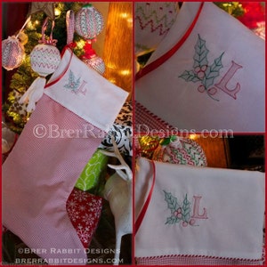 May include: A Christmas stocking featuring a red and white gingham pattern on the lower section and a white cuff. The cuff is embroidered with a green holly leaf design, red berries, and the letter L. The stocking has a red ribbon trim.