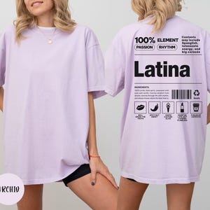 Może przedstawiać: Jasnofioletowa koszulka oversize z napisem "Latina" wydrukowanym na czarno z tyłu. Koszulka zawiera dodatkowy tekst i grafikę, w tym słowa "100% ELEMENT" i "PASSION RHYTHM". Z przodu nadrukowana jest nazwa marki "ORCHIO".