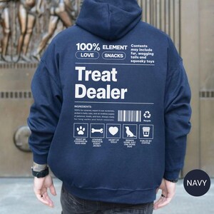 May include: Navy blue hoodie with the text "Treat Dealer" in white. The back of the hoodie features a list of ingredients and icons related to dogs, such as a paw print, bone, heart, dog silhouette, and coffee cup.