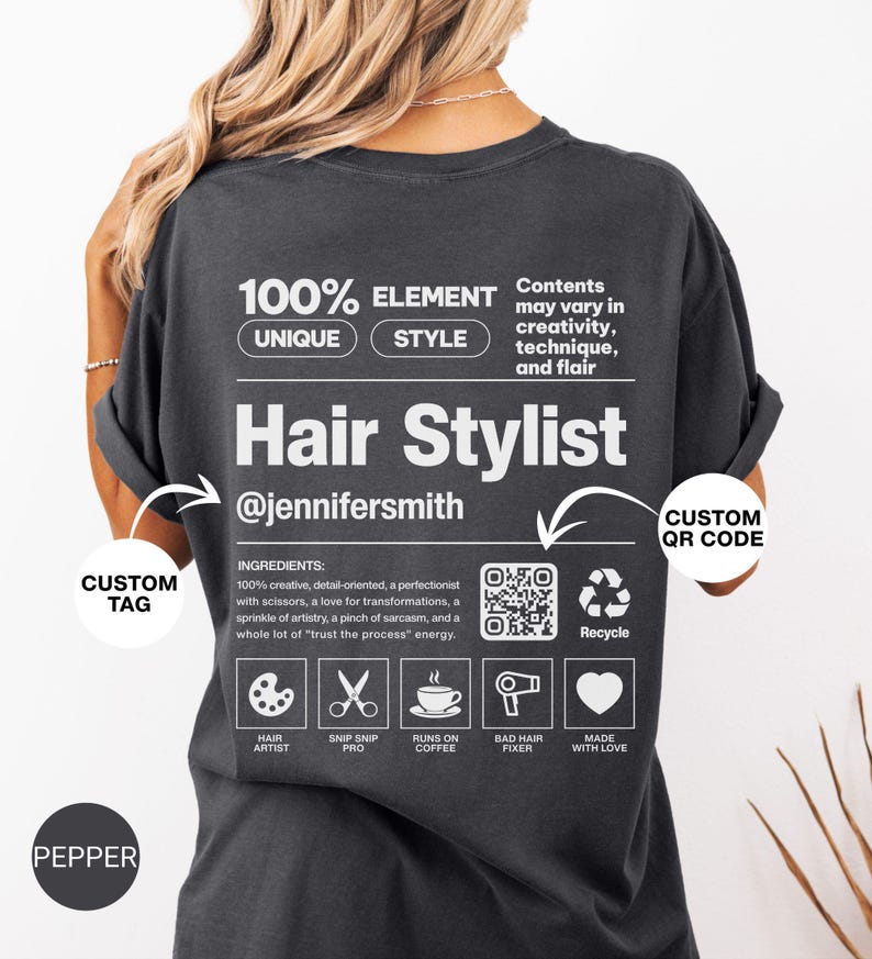 K&ouml;nnte beinhalten: Ein anthrazitfarbenes T-Shirt mit einer wei&szlig;en Grafik auf der R&uuml;ckseite, die einem Produktetikett &auml;hnelt. Der Text lautet 100% ELEMENT UNIQUE STYLE, Hair Stylist, @jennifersmith, inklusive Inhaltsstoffen, QR-Code und f&uuml;nf Symbolen.