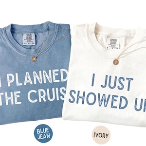 May include: Two crew neck t-shirts with Comfort Colors labels. The blue jean shirt features white text reading I PLANNED THE CRUISE. The ivory shirt features blue text reading I JUST SHOWED UP. Both shirts include a thin gold-toned necklace.