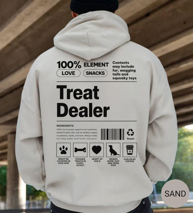 May include: Sand-colored hoodie with the text "Treat Dealer" in large black letters. The back of the hoodie features a list of ingredients and icons related to dogs, including a paw print, bone, heart, dog silhouette, and coffee cup.