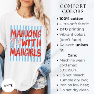 Peut inclure: Un t-shirt blanc avec un carr&eacute; &agrave; rayures verticales bleues portant le texte rouge MAHJONG WITH MAHGIRLS et une petite ic&ocirc;ne de tuile de mahjong rouge. Le t-shirt est en 100% coton, pr&eacute;sente une coupe d&eacute;contract&eacute;e et une impression DTG.