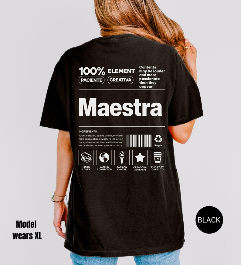 May include: A black t-shirt featuring a white graphic on the back with the text Maestra, 100% Element, Paciente, Creativa, and a list of ingredients including 100% corazon, spiced with humor, and icons representing a book, globe, torch, star, and coffee cup.