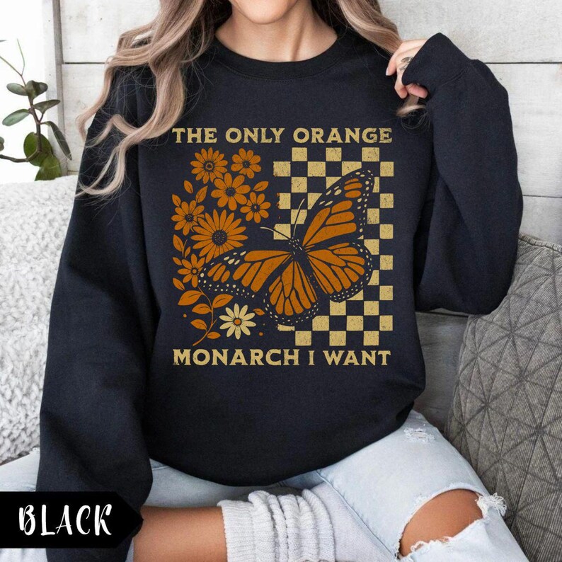 May include: Black sweatshirt with a graphic design featuring a monarch butterfly, flowers, and the text "THE ONLY ORANGE MONARCH I WANT." The design includes orange and yellow elements on a checkered background.