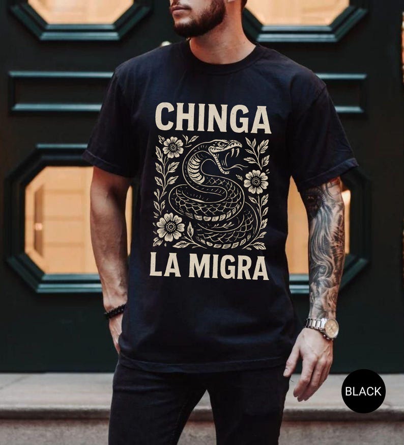 Puede incluir: Camiseta negra con un dise&ntilde;o de serpiente y el texto "CHINGA LA MIGRA" en una fuente decorativa. La serpiente est&aacute; rodeada de elementos florales. La camiseta es de cuello redondo.