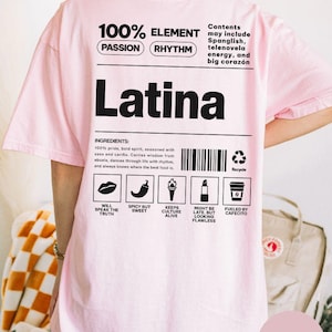 Może przedstawiać: Jasnor&oacute;żowa koszulka z napisem "Latina" dużymi czarnymi literami. Koszulka zawiera tekst i grafikę, w tym "100% Element" i ikony składnik&oacute;w. Na koszulce znajduje się r&oacute;wnież napis "Blossom".