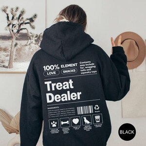 May include: Black hoodie with the text "Treat Dealer" and other text including "100% Love Snacks" and "Contents may include fur, wagging tails and squeaky toys". The hoodie has a hood and a kangaroo pocket.