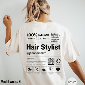 K&ouml;nnte beinhalten: Ein elfenbeinfarbenes T-Shirt mit einer schwarzen Grafik auf der R&uuml;ckseite, die einem Produktetikett &auml;hnelt. Es enth&auml;lt den Text Hair Stylist, @jennifersmith, eine Zutatenliste, einen QR-Code sowie Symbole f&uuml;r Palette, Schere, Kaffee, F&ouml;hn und Herz.