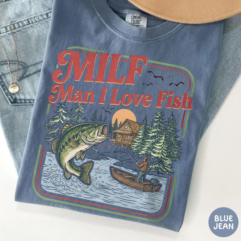May include: A blue Comfort Colors t-shirt with a graphic that reads "MILF Man I Love Fish" in red and orange. The graphic features a fish jumping out of the water, a fisherman in a boat, and a cabin in the woods.