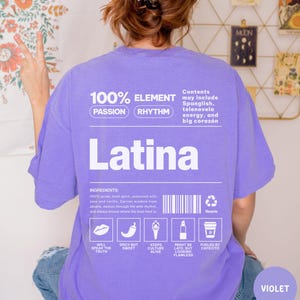 Może przedstawiać: Fioletowa koszulka z napisem "Latina" w kolorze białym. Koszulka zawiera tekst o dumie, duchu i kulturze, a także ikony i słowa "Passion" i "Rhythm". Codzienny element garderoby.