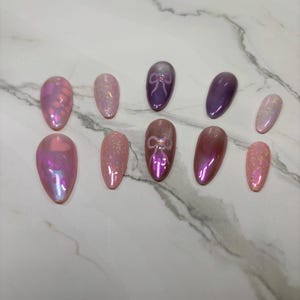 May include: Set of ten false nails with a variety of pink and purple iridescent finishes. Some nails have a small pink bow design.