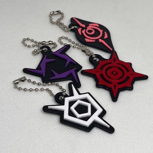 May include: Four black keychains with different colored symbols. The symbols are a purple star, a red sun, a white hexagon, and a pink rose.