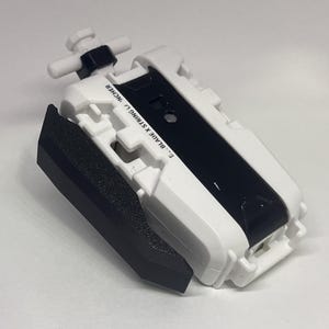 May include: A white and black toy launcher with the text "S.. BLADE X STRING L.. INCHER". The launcher has a black grip and a white handle. The toy is designed for launching a spinning top.