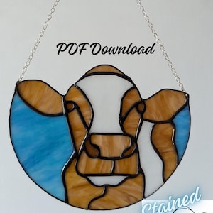 May include: A stained glass window hanging from a chain, featuring a brown and white cow's face. The glass is in shades of brown, white, and blue. The text "PDF Download" is visible above the cow. The text "Stained & Crafted" is visible below the cow.