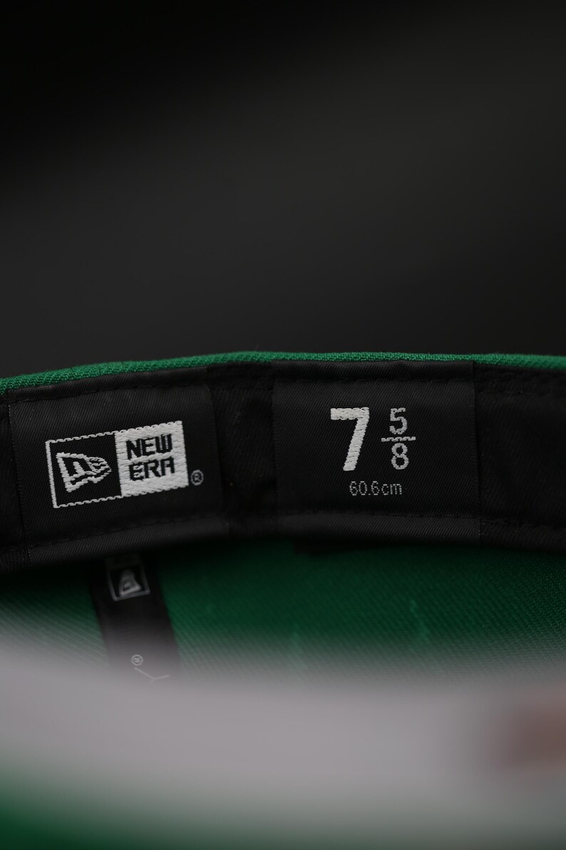 May include: Close-up of the interior of a green baseball cap. The black label displays the New Era logo and the size 7 5/8, equivalent to 60.6cm. The cap's interior is green.