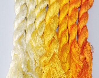 May include: A collection of silk threads in a gradient of yellow and orange hues. The skeins of thread are arranged side by side, transitioning from a pale cream color to vibrant shades of yellow and orange. The threads are tightly twisted, showcasing their texture.
