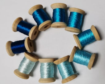 May include: A collection of wooden spools filled with vibrant blue and teal thread. The spools are arranged in a circular pattern, showcasing the different shades of thread. The wooden spools add a rustic touch to the colorful threads, creating a visually appealing display.