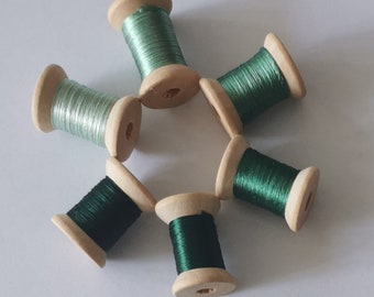 May include: Six wooden spools of green thread, arranged in a circular pattern. The spools have natural wood ends and are filled with shiny thread. The number "5#" is visible in the upper right corner.