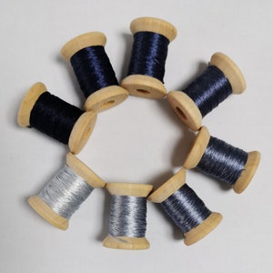 May include: A collection of wooden spools filled with navy blue and silver thread. The spools are arranged in a circular pattern, showcasing the different shades of thread. The wooden spools have a natural wood finish.