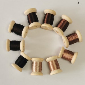 May include: A collection of wooden spools filled with various shades of thread, including black, brown, and copper. The spools are arranged in a circular pattern, showcasing the different colors and textures of the thread.