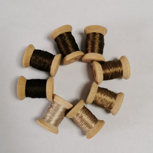 May include: A selection of wooden spools, each wound with thread in shades of brown, gold, and silver. The spools are arranged in a circle, displaying the different colours and textures of the thread. Suitable for sewing, embroidery, or craft projects.