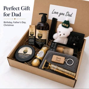 Könnte beinhalten: Eine Geschenkbox mit Bartspülung, Bartöl, Bart-Styler, einem schwarzen Kamm, einem weißen Teddybären mit grüner Mütze, einem Rasierpinsel, einer Ferrero Rocher Praline, einem grauen Handtuch, einem Schlüsselanhänger mit Best Dad Text und einem Goldtrimmer.