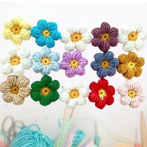 Könnte beinhalten: Sortiment an gehäkelten Blumenverzierungen in verschiedenen Farben, darunter Gelb, Blau, Weiß, Lila, Grün, Rot und Braun. Die Blumen sind alle gleich groß und haben die gleiche Form, mit fünf Blütenblättern und einer kleinen gelben Mitte.