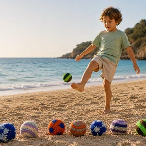Può includere: Un bambino calcia una palla all'uncinetto verde e nera su una spiaggia sabbiosa. Diverse palle all'uncinetto colorate sono allineate nella sabbia. L'oceano e una costa rocciosa sono sullo sfondo.