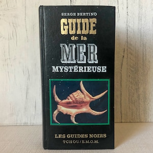 K&ouml;nnte beinhalten: Ein schwarzes Buch mit dem Titel "GUIDE de la MER MYSTERIEUSE" von Serge Bertino. Das Cover zeigt eine Muschelillustration in einem gr&uuml;nen Rahmen. Teil der Reihe "LES GUIDES NOIRS".