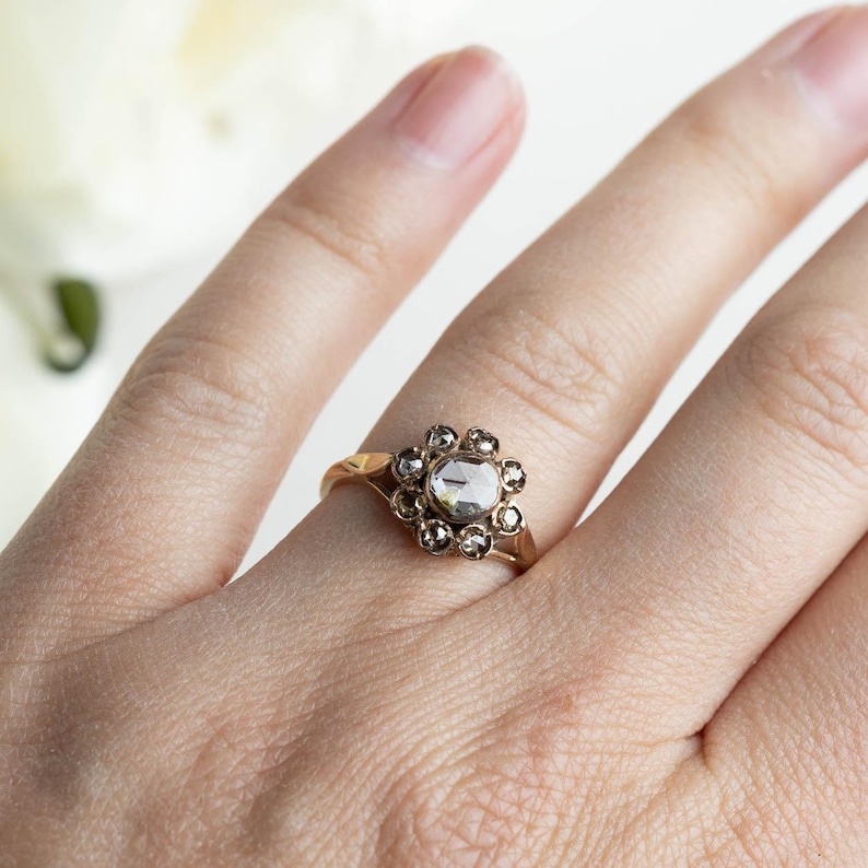 May include: A gold ring with a large, clear, faceted gemstone surrounded by a halo of smaller, faceted gemstones.
