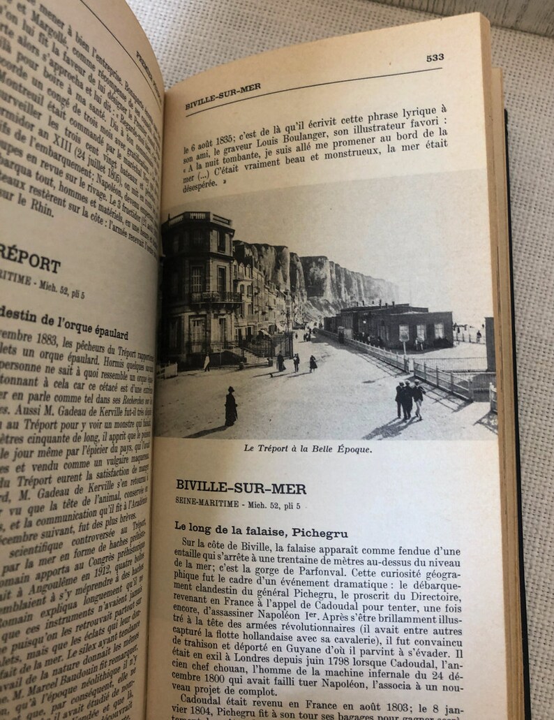 K&ouml;nnte beinhalten: Ein offenes Buch mit Text und einer Schwarz-Wei&szlig;-Fotografie einer K&uuml;stenlandschaft. Das Foto zeigt Geb&auml;ude, Klippen und Menschen. Der Text ist auf Franz&ouml;sisch.
