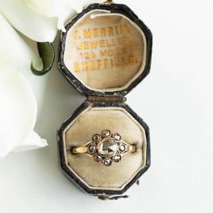 May include: A vintage ring with a large, faceted, rose-cut diamond surrounded by smaller diamonds. The ring is set in gold and is in a black velvet ring box. The box is inscribed with "J. Merrill Jeweller 124 Moor Sheffield."