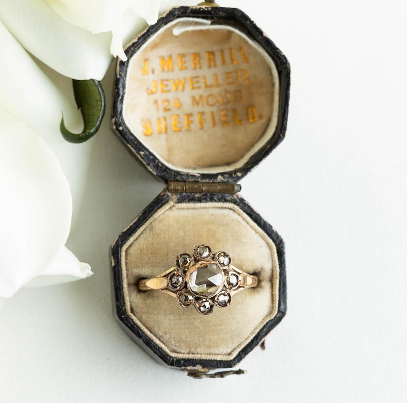 May include: A vintage ring with a large, faceted, rose-cut diamond surrounded by smaller diamonds. The ring is set in gold and is in a black velvet ring box. The box is inscribed with "J. Merrill Jeweller 124 Moor Sheffield."