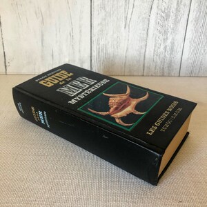 K&ouml;nnte beinhalten: Ein schwarzes Buch mit dem Titel "GUIDE de la MER Myst&eacute;rieuse" mit goldener Schrift und einer Muschelillustration. Das Buch geh&ouml;rt zur Reihe "LES GUIDES NOIRS". Der Buchr&uuml;cken zeigt ebenfalls den Titel. Das Buch liegt auf einer hellbeigen Oberfl&auml;che.