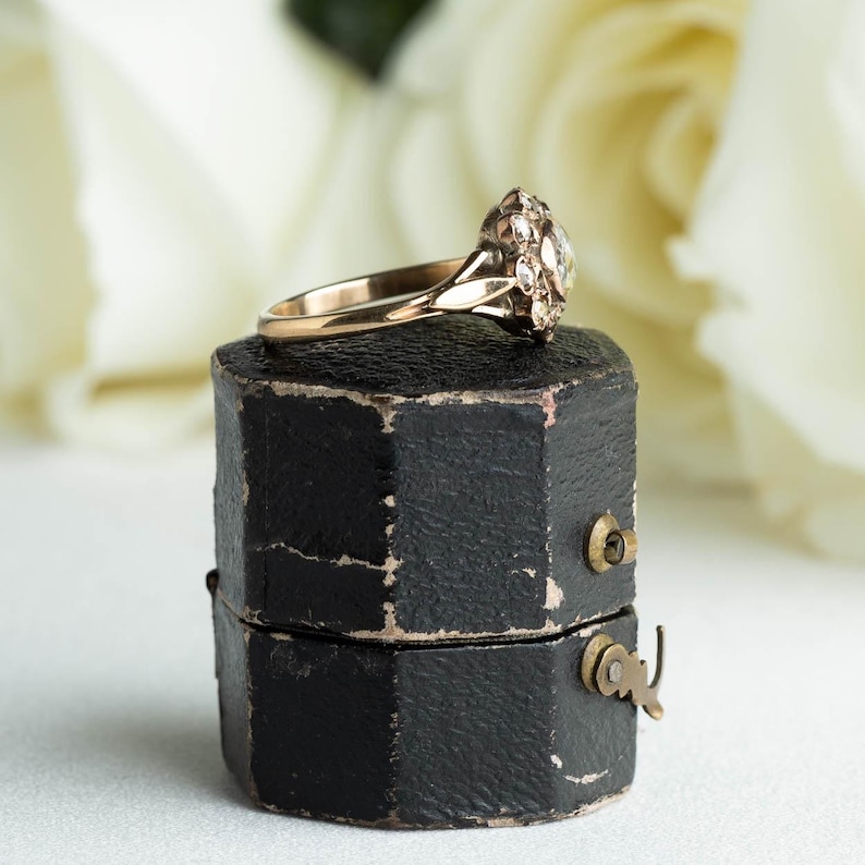 May include: A vintage engagement ring with a cluster of small diamonds set in a gold band, displayed in a black ring box.