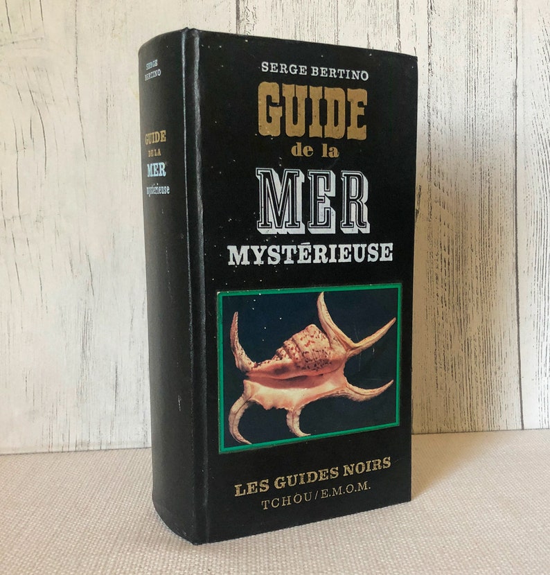 K&ouml;nnte beinhalten: Ein schwarzes Hardcover-Buch mit dem Titel "GUIDE de la MER MYSTERIEUSE" von Serge Bertino. Das Cover hat goldene und wei&szlig;e Schrift und eine Muschelabbildung. Das Buch geh&ouml;rt zur Reihe "LES GUIDES NOIRS".